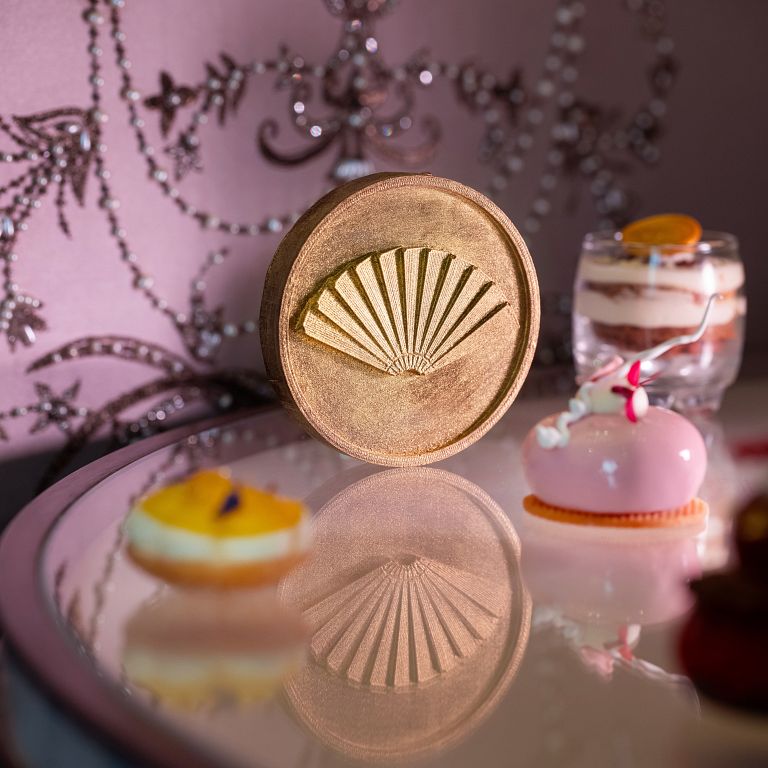 巧克力焦糖堅果瑪德蓮: 外層以 58%黑巧克力製成,口感酥脆,中間夾入杏仁與榛果醬,底部則搭配焦糖瑪德蓮,外型製成酒店集團標誌性的摺扇,整體帶有醇厚的焦糖與黑巧克力香氣。(圖/台北文華東方酒店 提供)